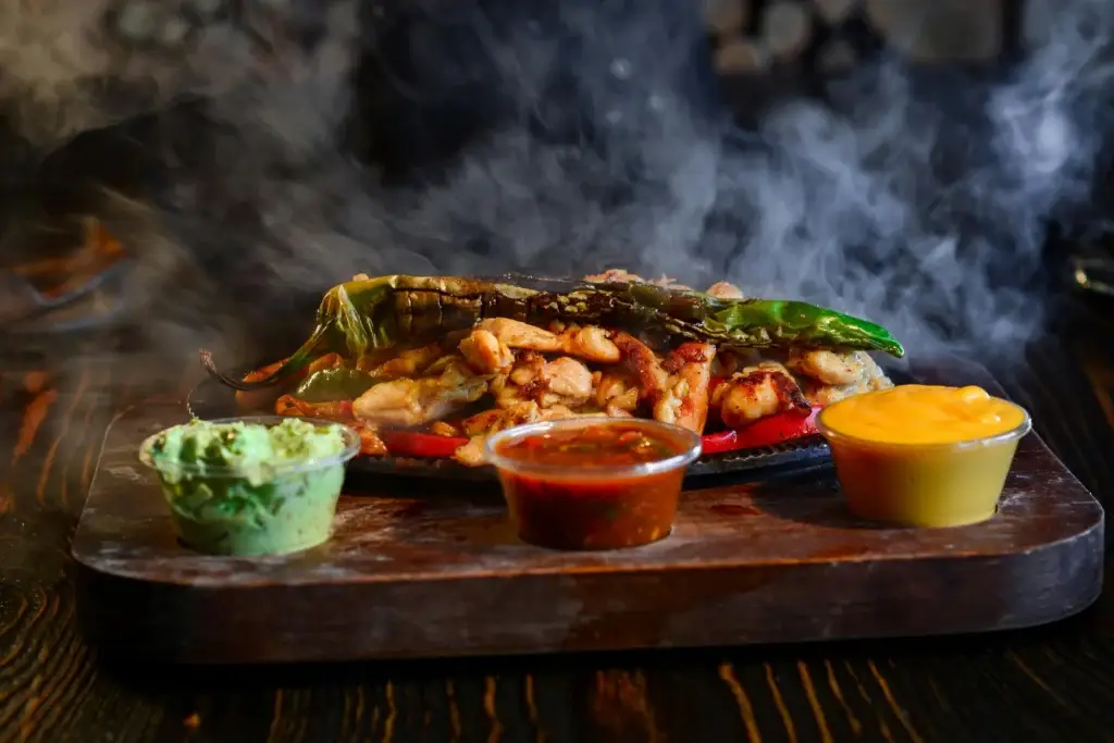 Delicious sizzling fajitas served with guacamole, salsa, and cheesy sauce on a wooden tray.